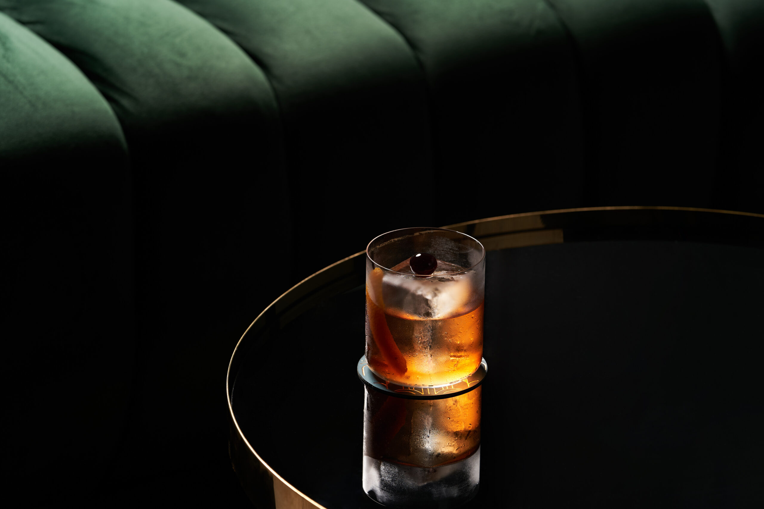 Two iced cocktails with cherries in moody bar light