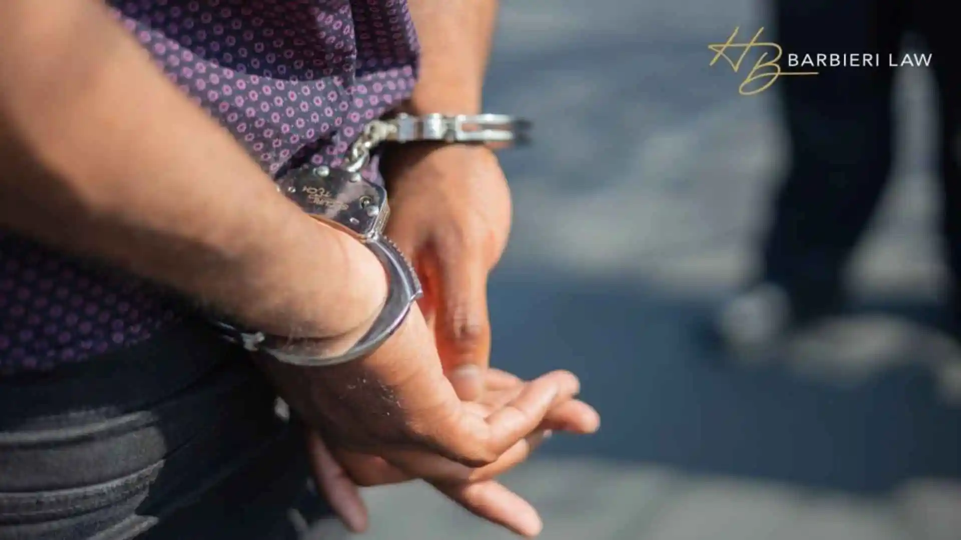 Close-up of an individual's hands in handcuffs, symbolizing arrest or crime, illustrating homicide lawyer in Allen TX. Branded with the Barbieri Law Firm, P.C. logo.